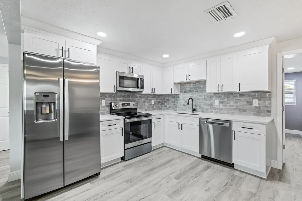 White kitchen with stainless appliances, stone mosaic backsplash and quartz counters