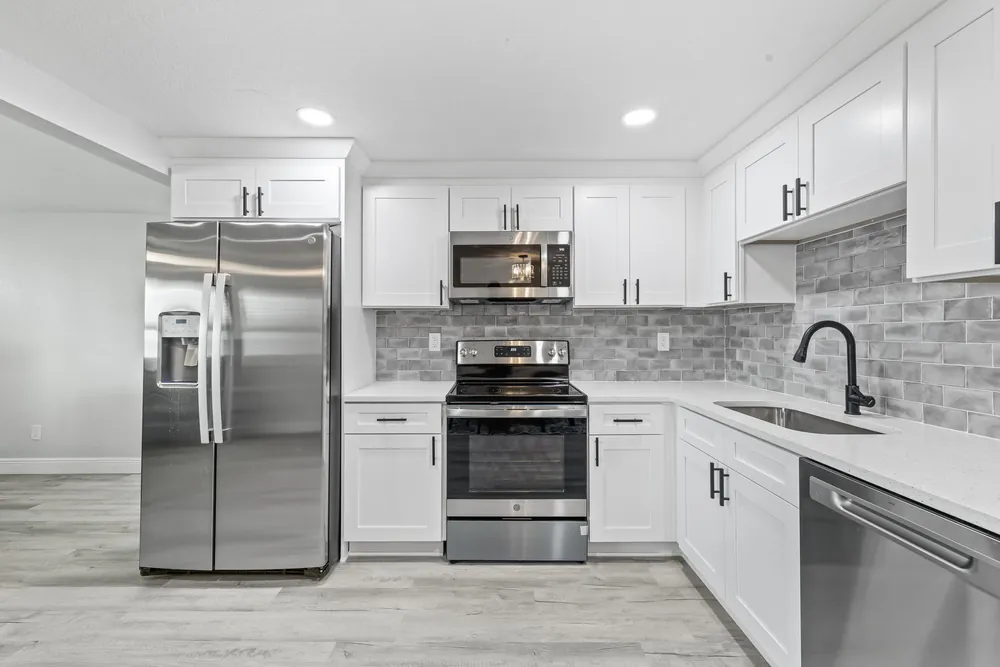 L-shaped white kitchen with stainless appliances and a grey stone backsplash