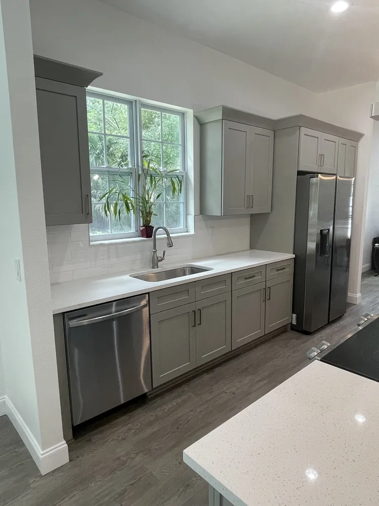 Kitchen with grey shaker cabinets, white quartz counters and stainless appliances by a window