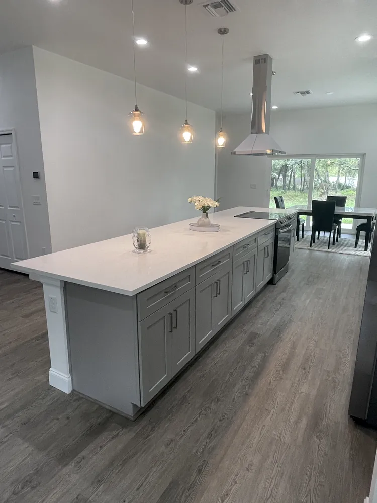 Open-plan kitchen with a long grey island, pendant lighting and plank floor